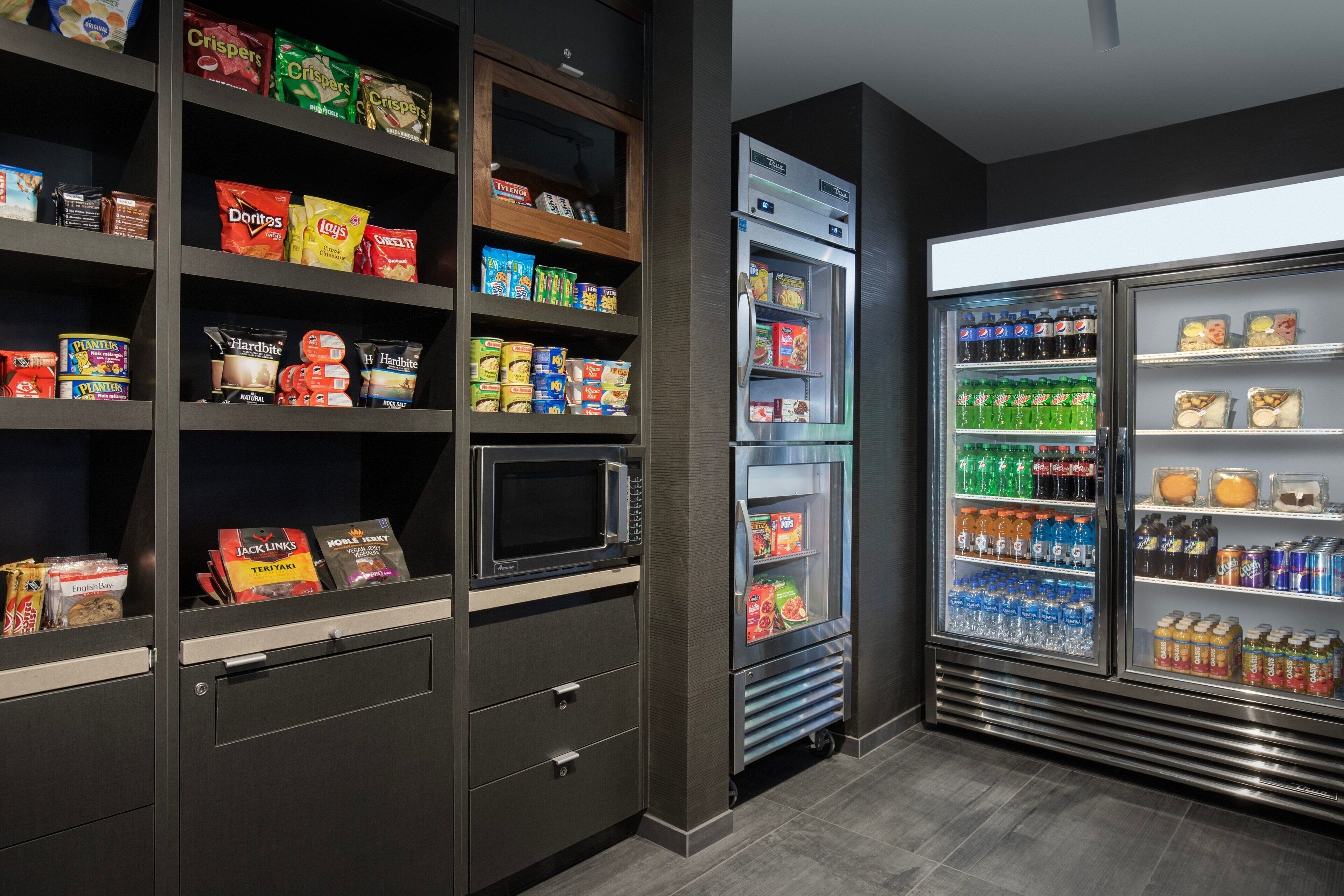 Un espace de libre-service où l’on peut trouver des collations et des boissons, avec des étagères remplies de produits, un four à micro-ondes et un réfrigérateur contenant diverses boissons.