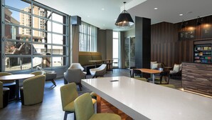 A modern interior with a long communal table, several chairs, a bar area, and large windows offering a view of the cityscape. - Courtyard By Marriott Nanaimo (Nanaimo)