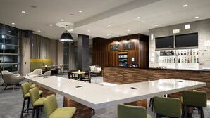 A modern bar area with a long white counter, green bar stools, and a wooden accent wall. - Courtyard By Marriott Nanaimo (Nanaimo)