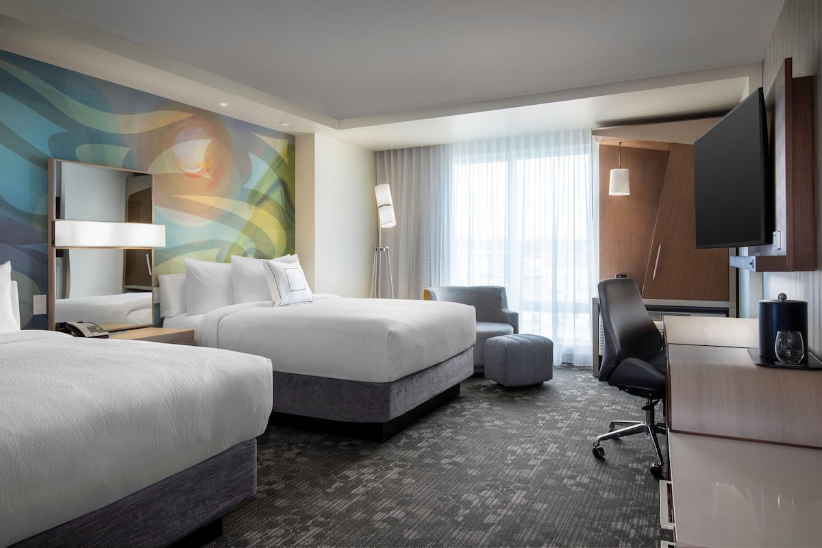 Een hotelkamer met twee bedden, een bureau, een stoel, een televisie en een groot raam met gordijnen.
