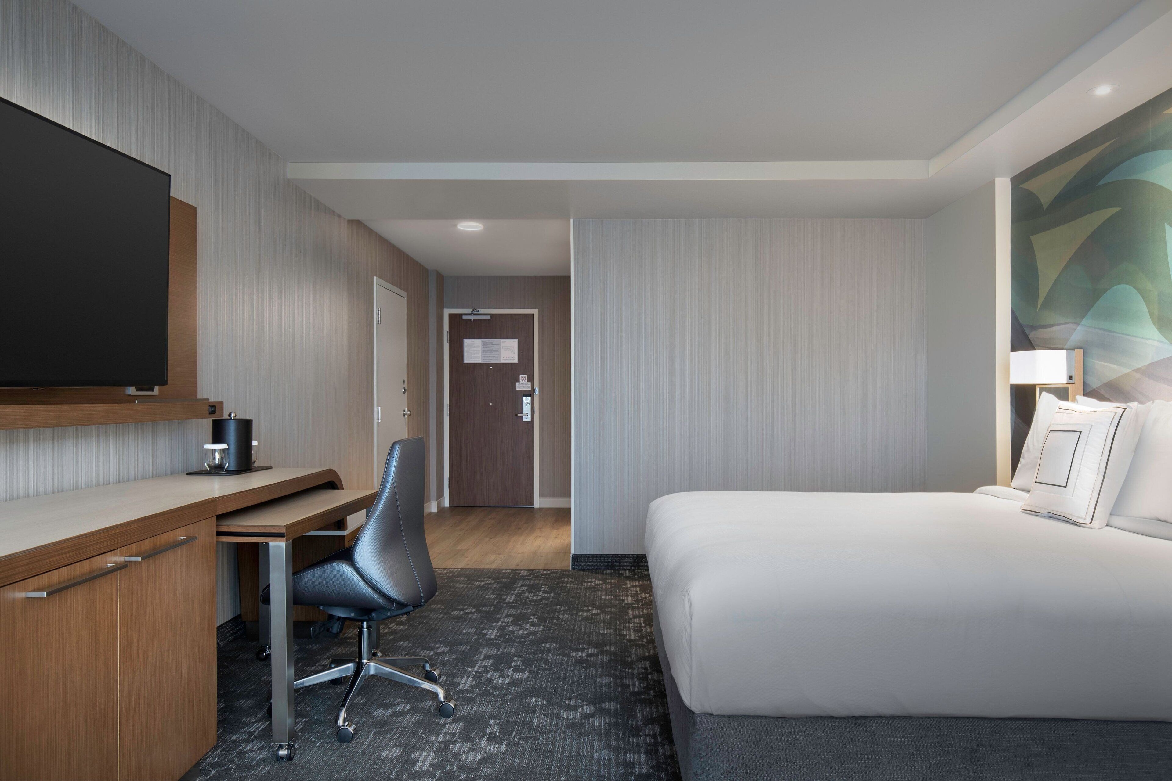 A hotel room with a bed, desk, chair, and a flat-screen TV.