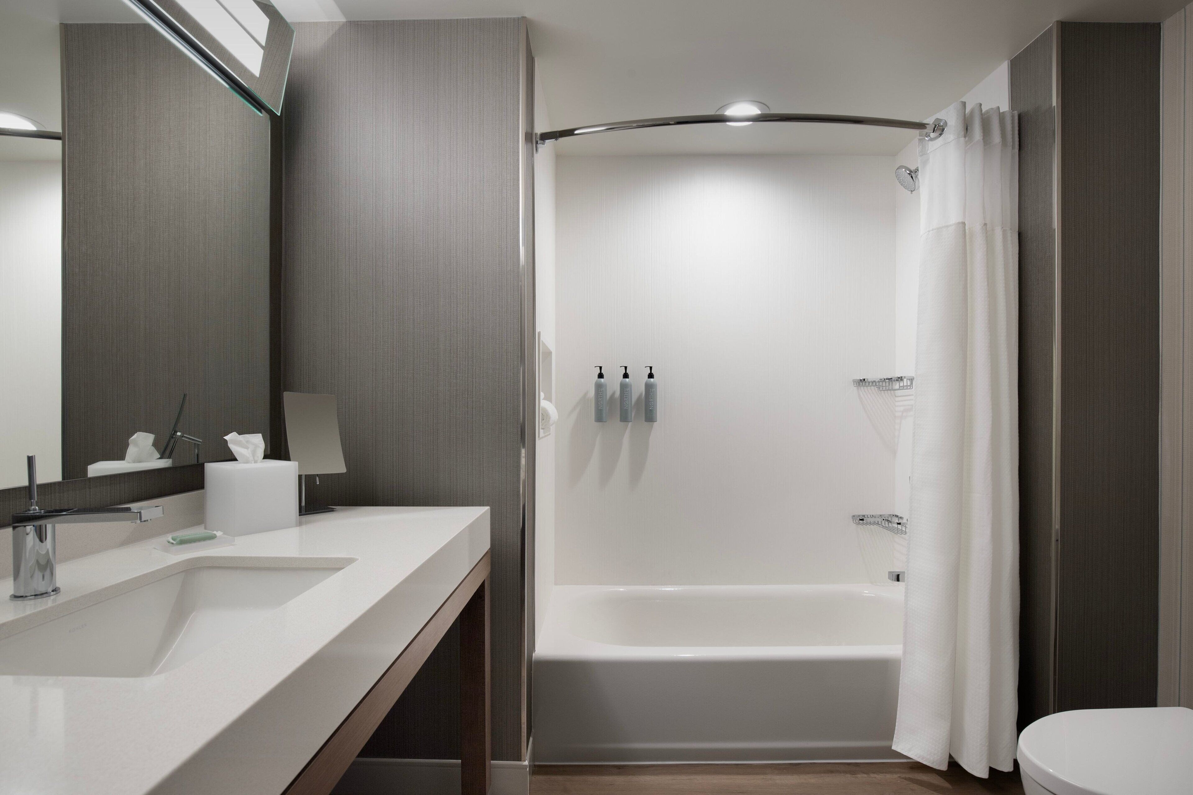 A modern bathroom with a white sink, mirror, and bathtub.