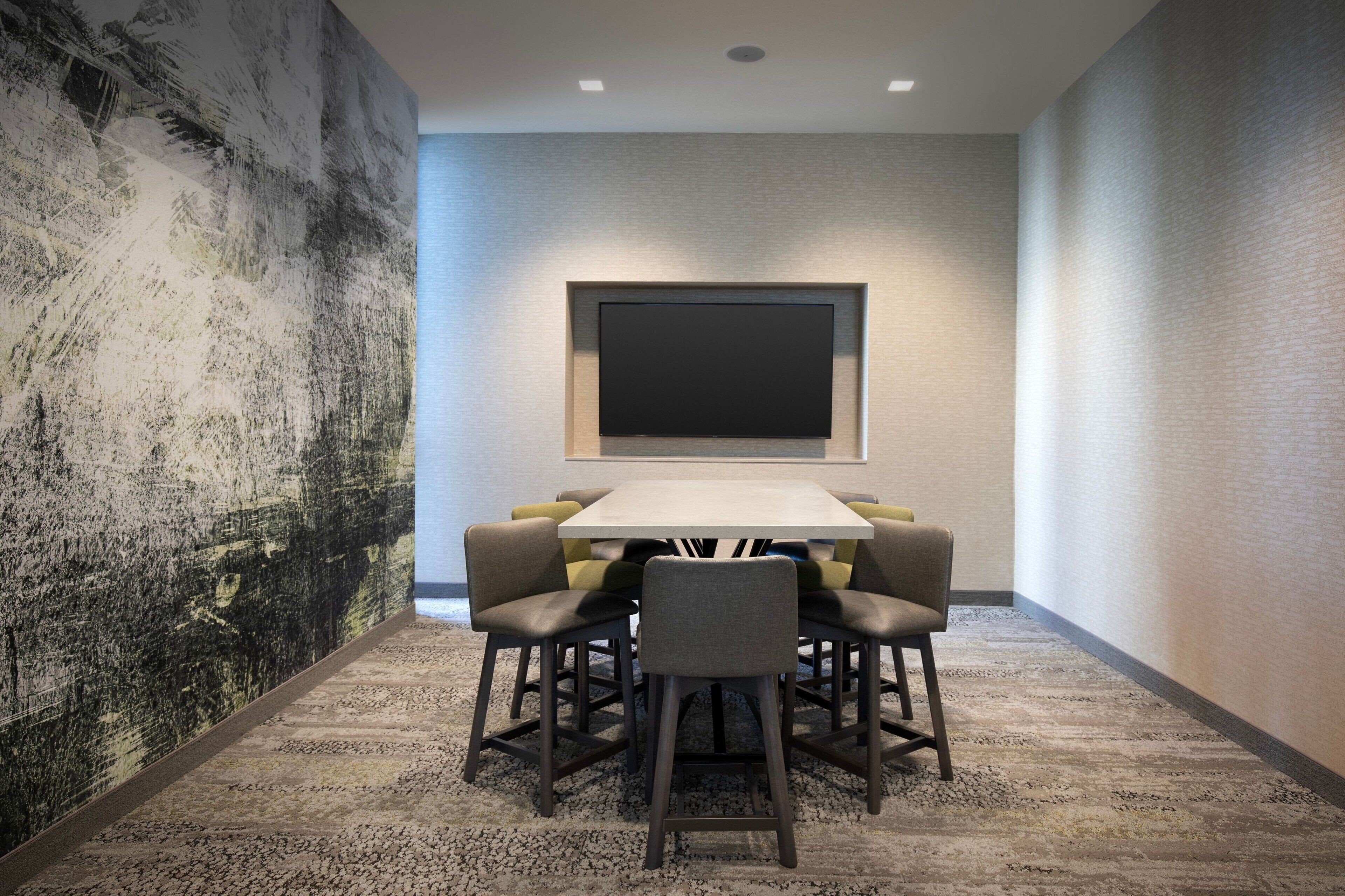 A conference room with a large table, six chairs, and a projector screen on the wall.