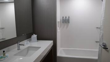 Un baño moderno con un espejo grande, dos lavamanos, una bañera y artículos de aseo en la pared.