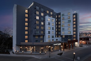A Courtyard hotel with a modern design, featuring multiple floors, large windows, and a well-lit entrance.