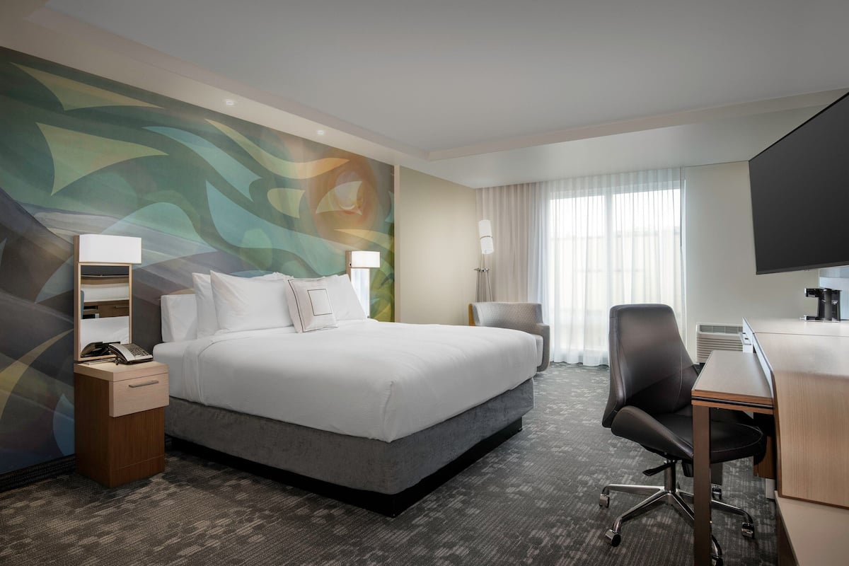 Een hotelkamer met een groot bed, een bureau, een stoel, een televisie, een lamp en een muur met een kleurrijk abstract ontwerp.