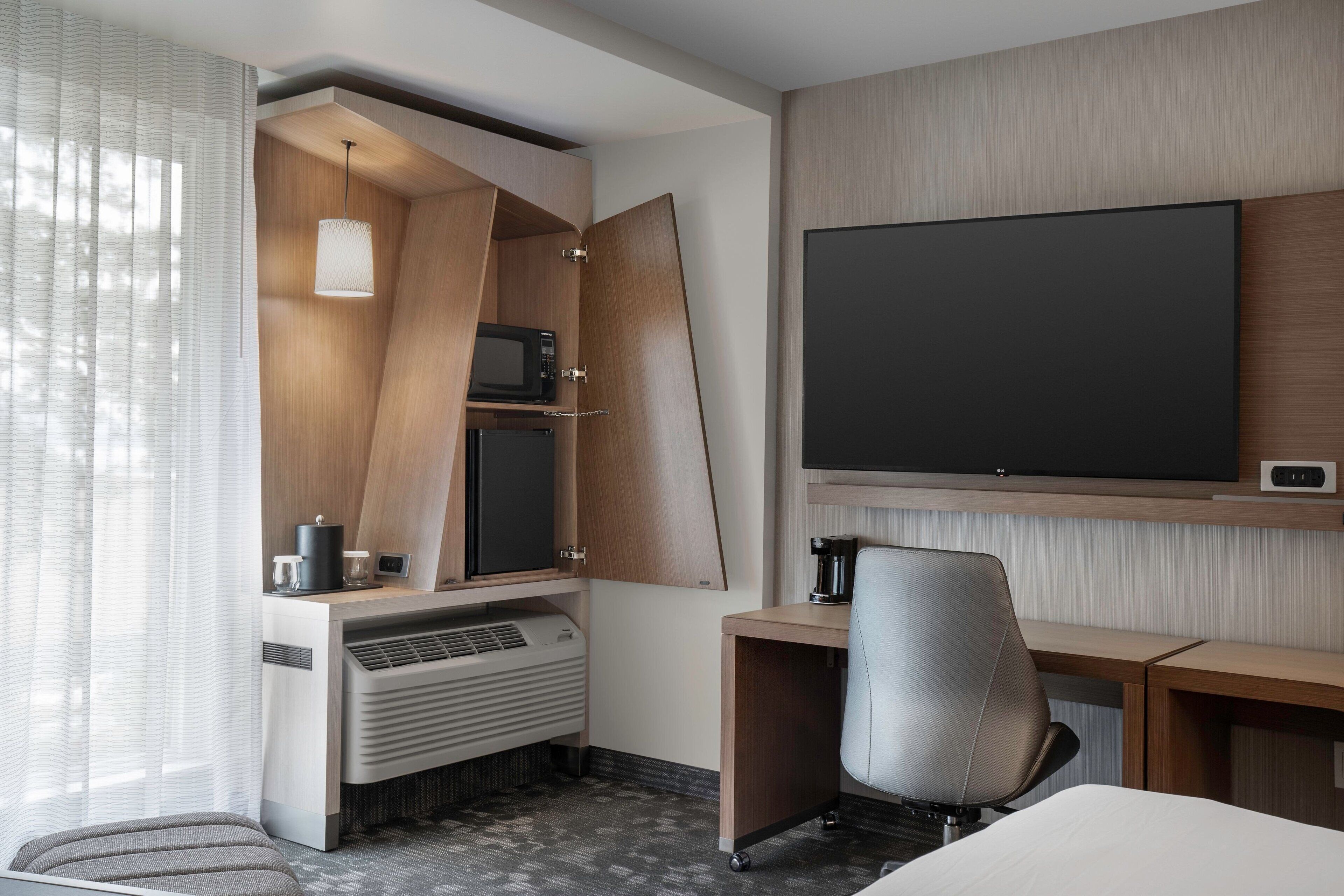 Una habitación de hotel moderna con televisión de pantalla plana, un escritorio con silla, microondas y cafetera.