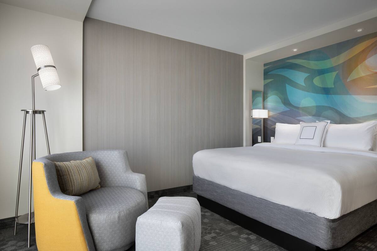 Een hotelkamer met een groot bed, een stoel, een vloerlamp en een gestructureerde muur.
