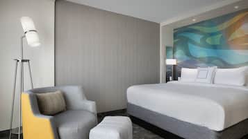 A hotel room with a large bed, a chair, a floor lamp, and a textured wall.