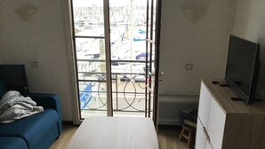 Une pièce comprenant un lit, un canapé bleu, un téléviseur et donnant sur une marina grâce à une porte vitrée.