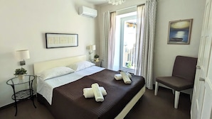 A hotel room with a bed, a chair, a table, a lamp, a painting, and a window with curtains. - The White House, terrace on the Mediterranean (Pozzallo)