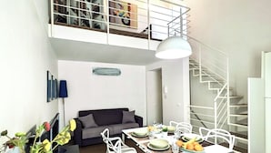 A dining area with a white table set for four, a sofa, and a staircase leading to an upper level. - The White House, terrace on the Mediterranean (Pozzallo)