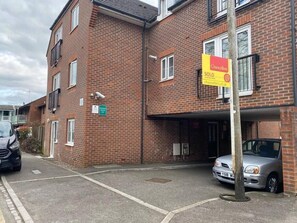 Un immeuble de deux étages en briques, sur lequel on peut lire une pancarte « VENDU », avec une voiture garée dans l’allée et un petit panneau indiquant un parking à proximité.