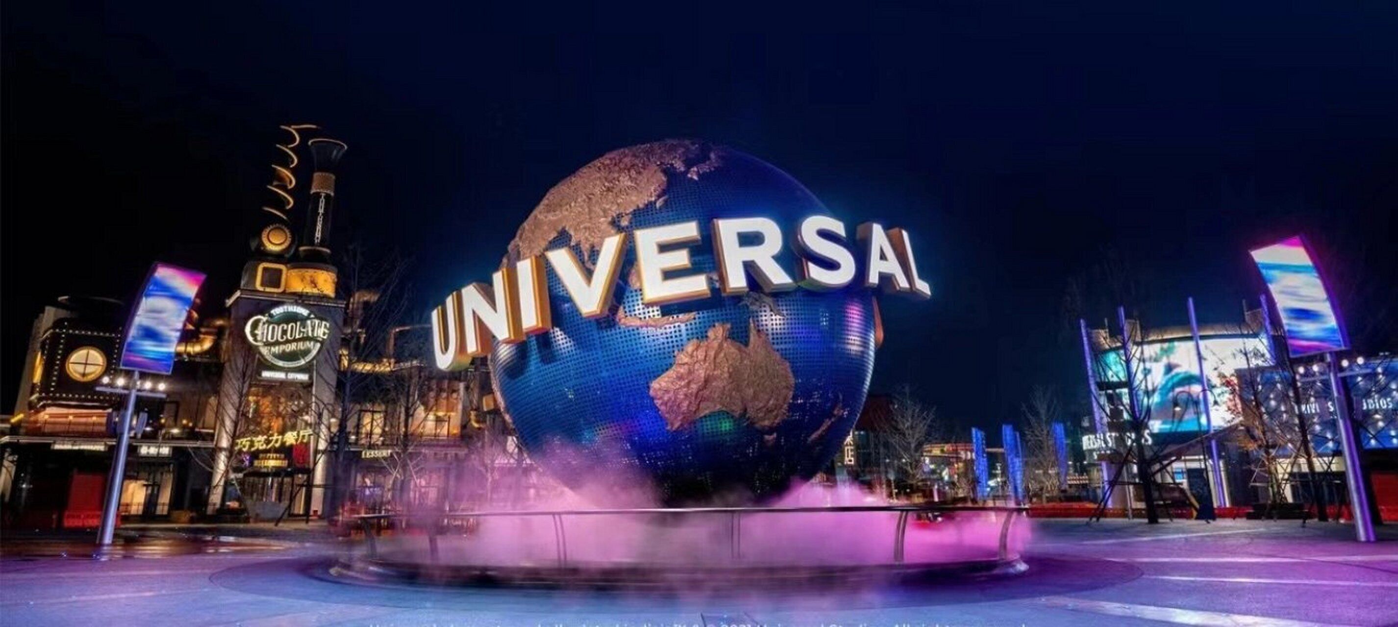 A large illuminated globe with the word "UNIVERSAL" in front of a building at night.