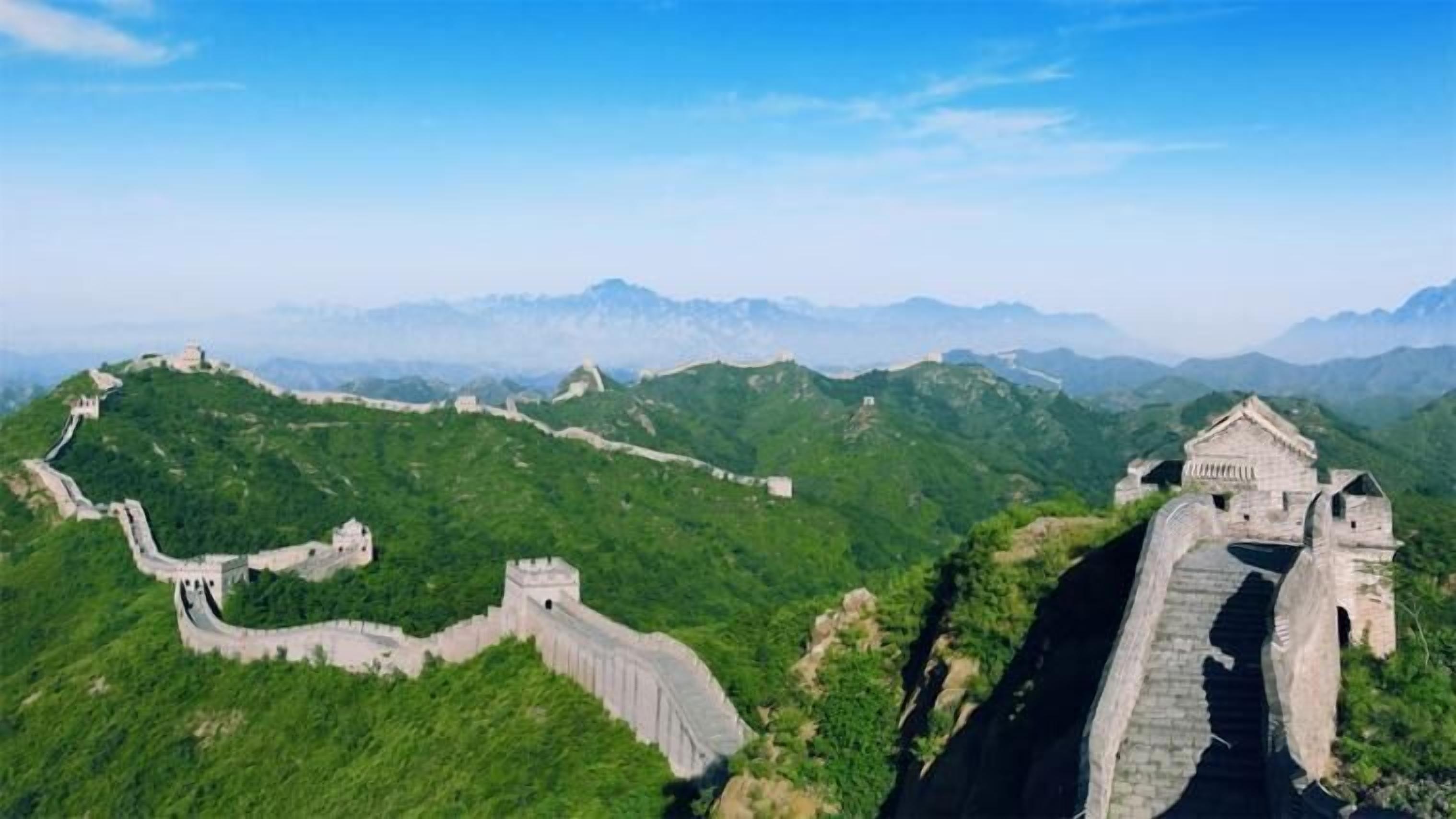 La Grande Muraglia Cinese serpeggia attraverso dolci colline verdeggianti, con una torretta di guardia e un tratto del muro in primo piano.