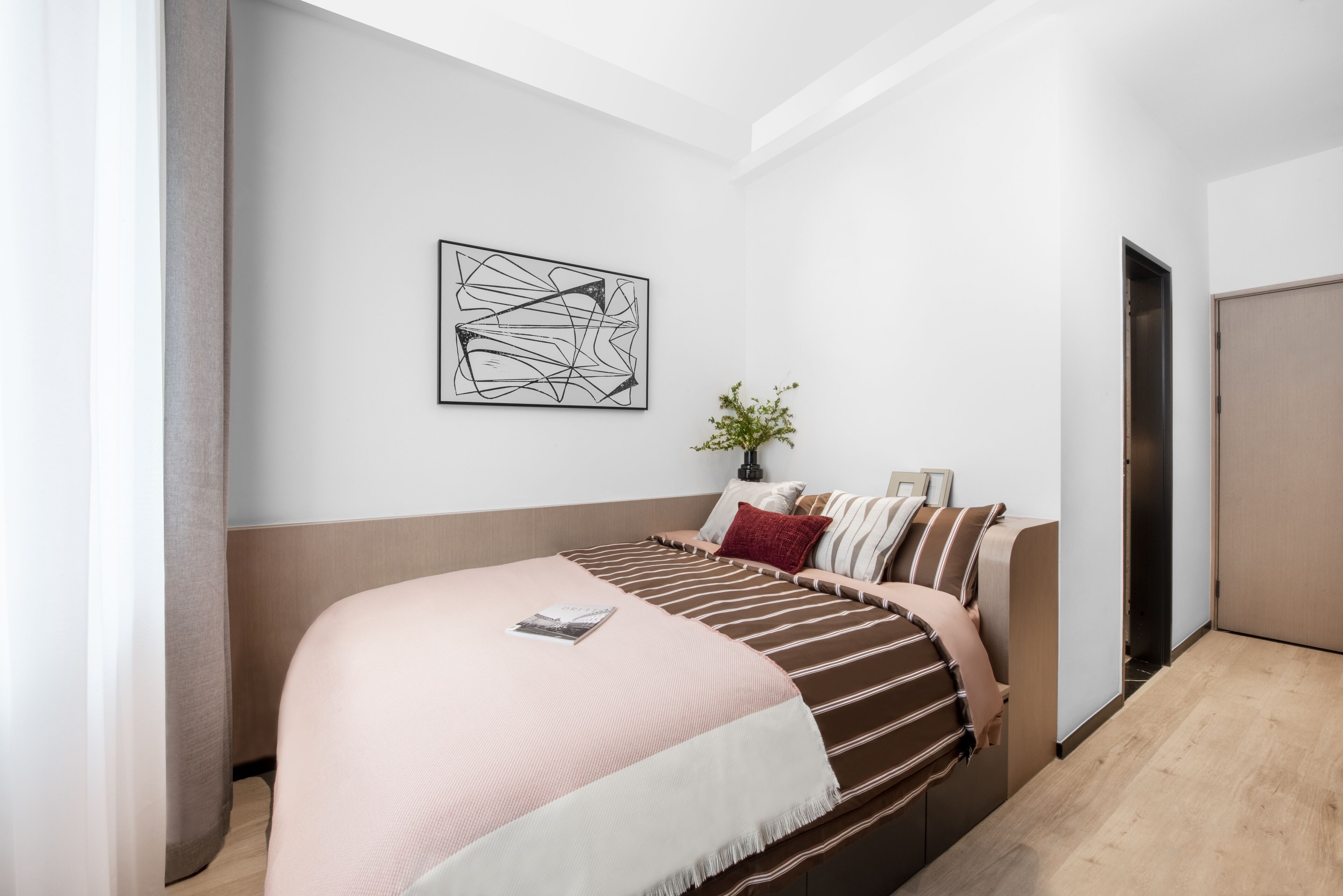 Quarto moderno com cama, obra de arte abstrata na parede, planta na mesa de cabeceira e uma porta.