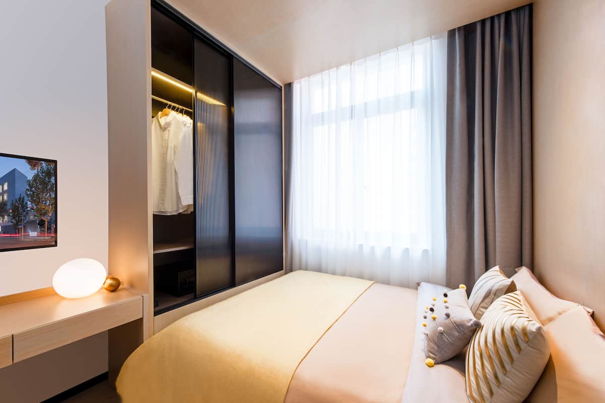Una habitación de hotel moderna con una cama, mesita de noche y un armario.