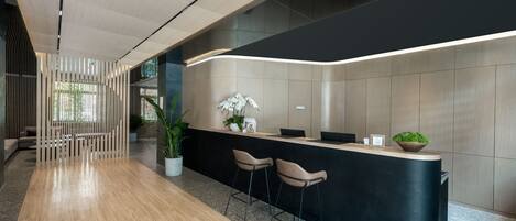 A modern reception area with a curved black counter, two bar stools, a potted plant, and a wooden floor.