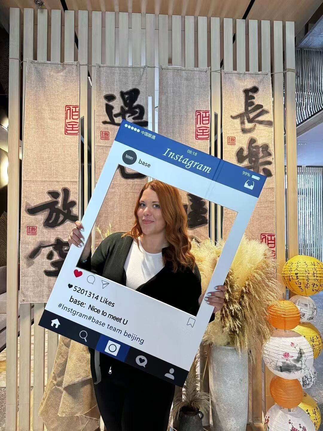 Una persona sosteniendo un cartel con una publicación de Instagram, de pie frente a una pared con caracteres chinos y faroles decorativos.