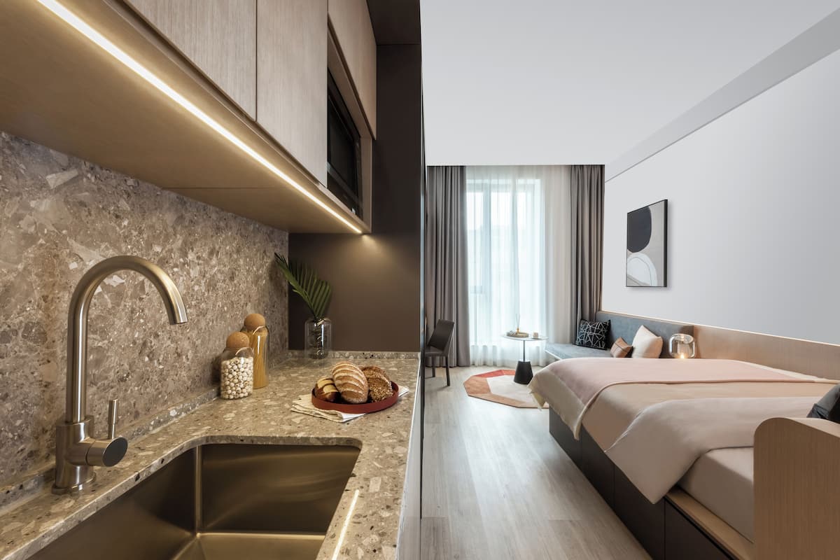 Una habitación de hotel moderna con cocina, cama con vistas y una pequeña zona de estar.