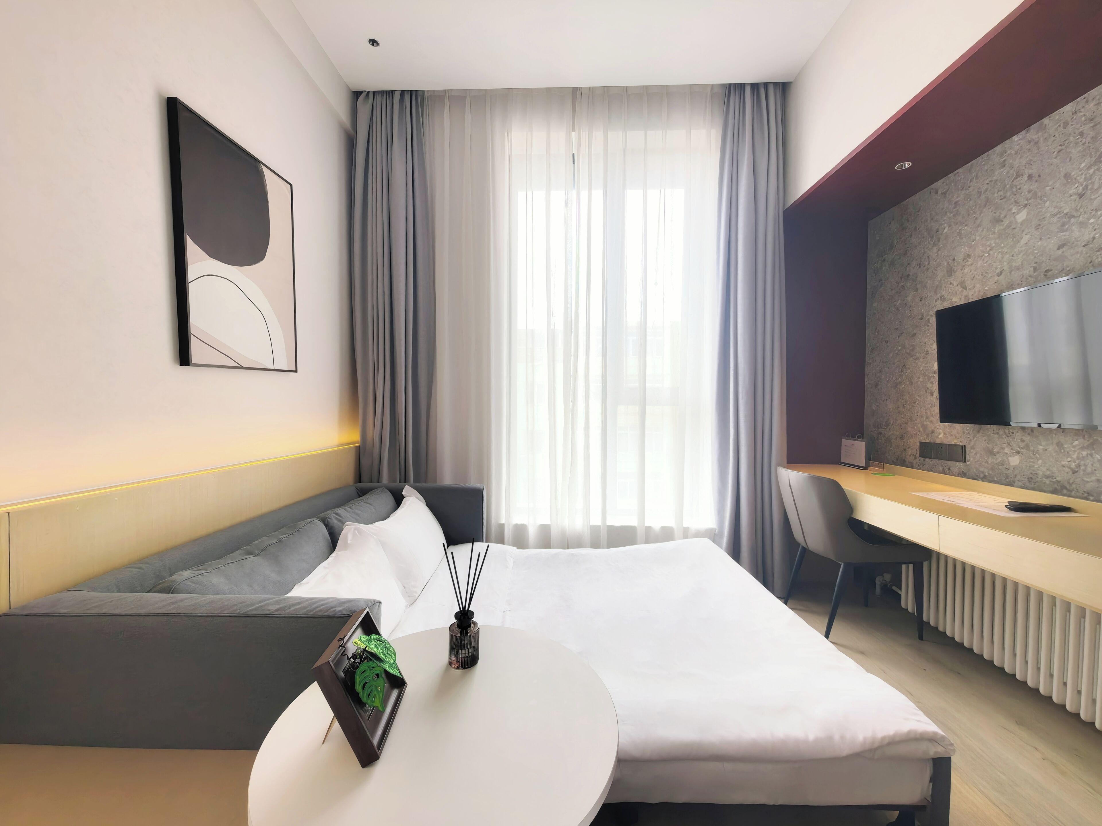 Une chambre d’hôtel moderne équipée d’un lit, d’un bureau, d’une télévision et d’une grande fenêtre avec des rideaux.