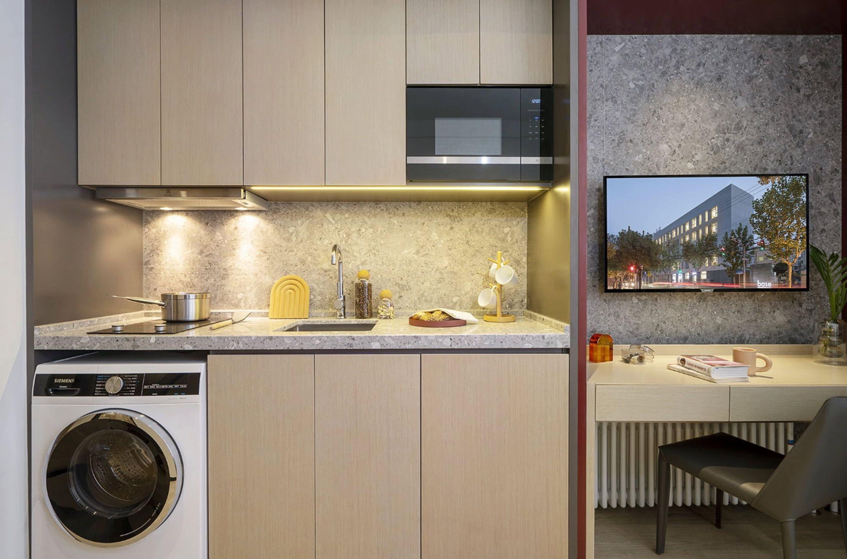 Cocina compacta con lavadora, microondas y un pequeño comedor con una silla y una mesa.