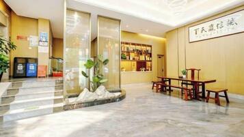 A hotel lobby with a reception desk, seating area, and a staircase leading to an upper level.
