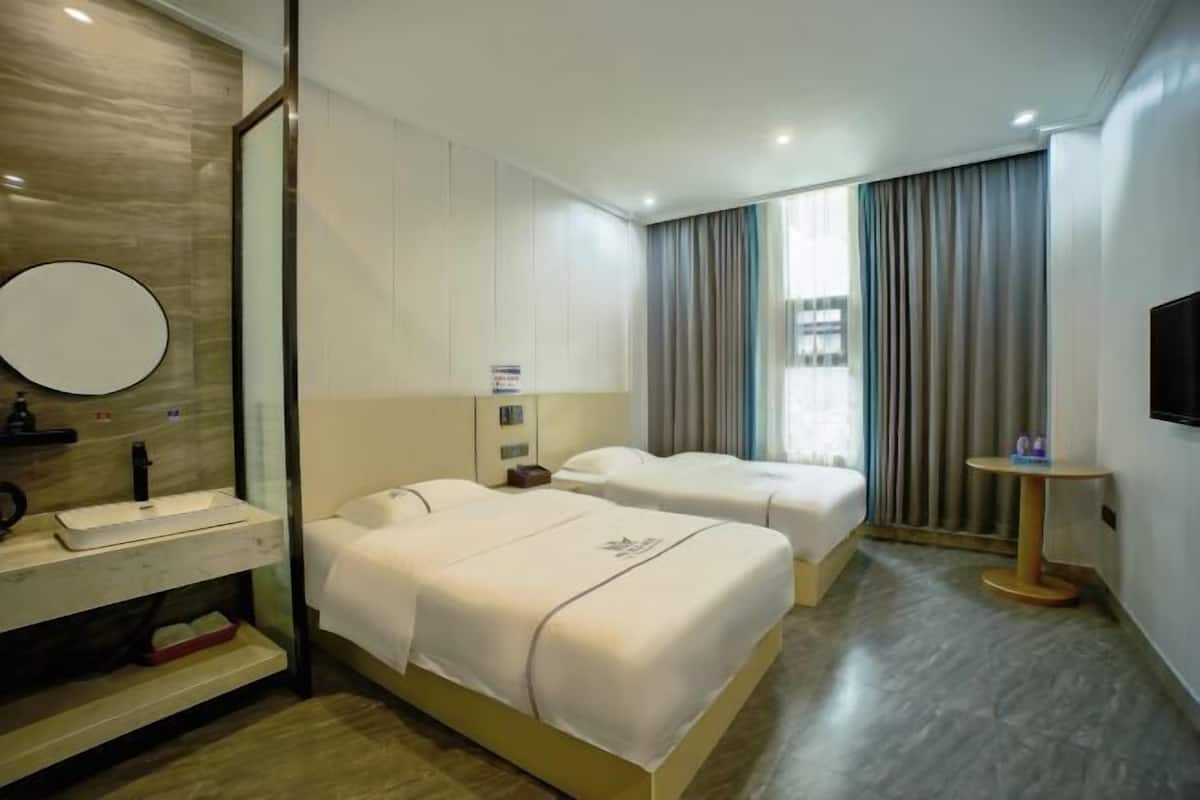 A hotel room with two beds, a round mirror, a small table, and a TV.