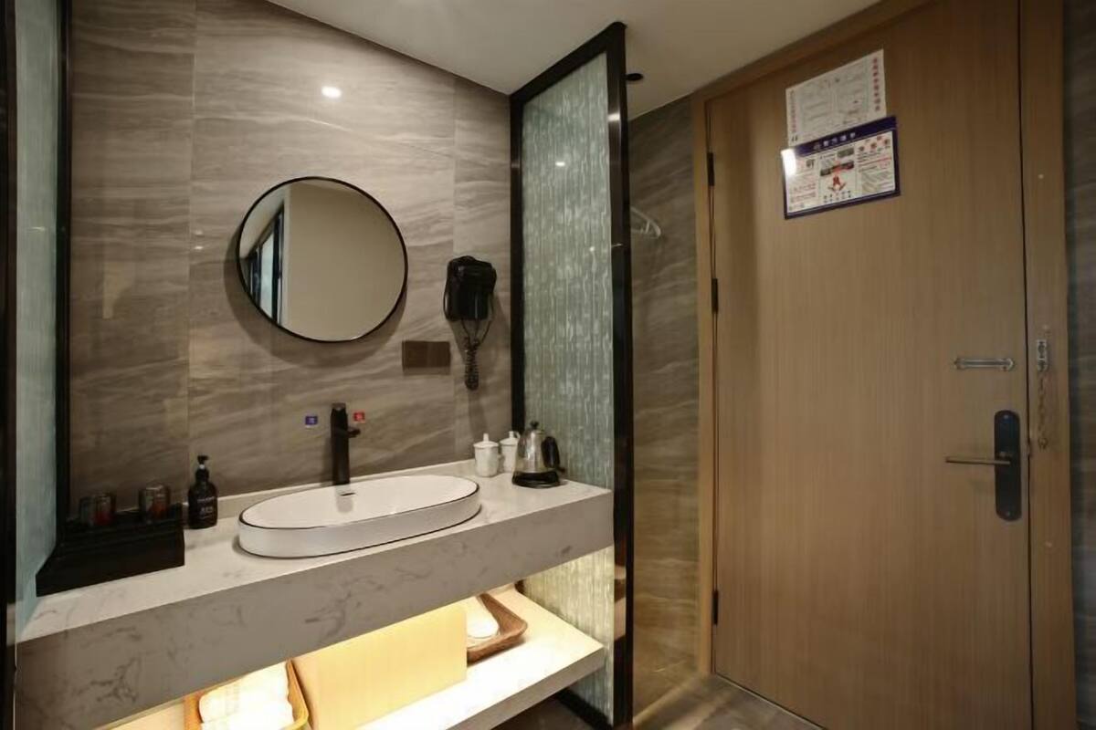 A modern bathroom with a marble sink, a round mirror, and a wooden door.