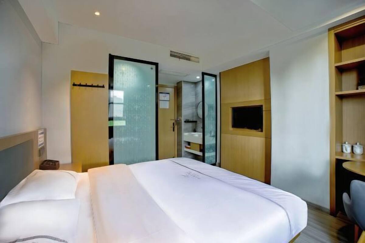 A hotel room with a large bed, a desk, a chair, and a TV.