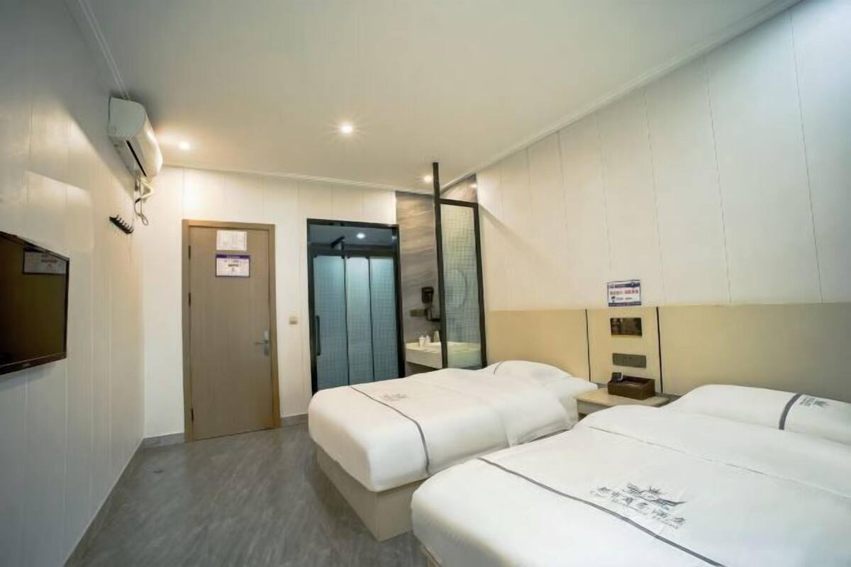 A hotel room with two beds, a shower area, a mirror, and a television.