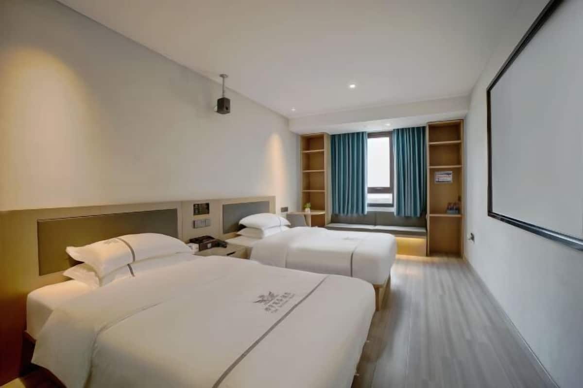 A hotel room with two beds, a large window with curtains, a TV, and a minibar.