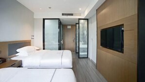 Une chambre d’hôtel moderne dotée d’un grand lit, d’un téléviseur fixé au mur et d’une porte coulissante donnant sur un couloir.