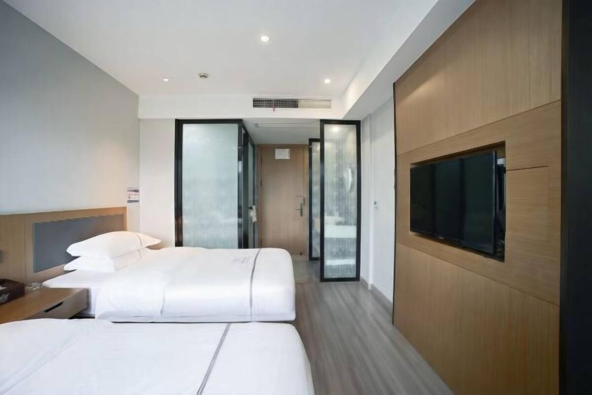 A modern hotel room with a large bed, a TV mounted on the wall, and a sliding door leading to a hallway.