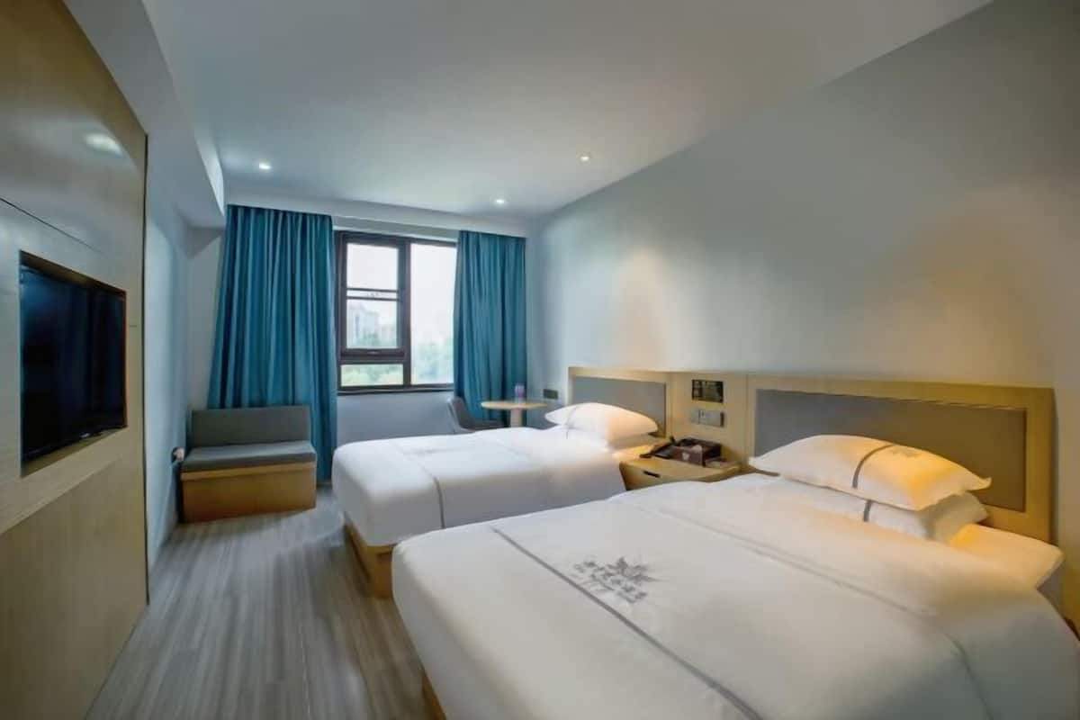 A hotel room with two beds, a TV, a desk, and a window with curtains.