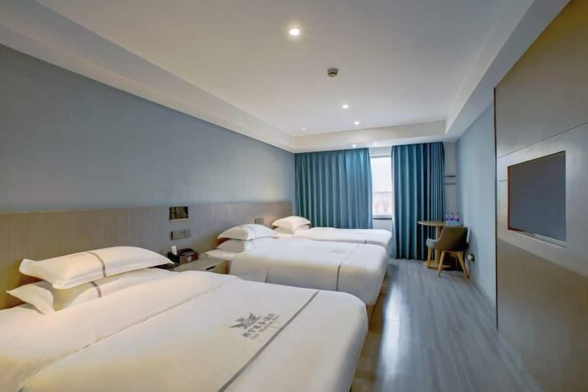 A hotel room with two beds, a small table, a chair, a TV, and a window with curtains.