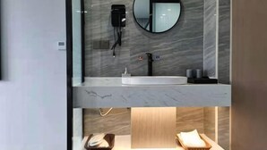 Une salle de bain moderne avec un meuble-lavabo en marbre, un miroir rond, un sèche-cheveux et un porte-serviettes.
