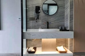 A modern bathroom with a marble vanity, a round mirror, a hairdryer, and a towel rack.