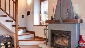 A cozy living room with a fireplace, wooden staircase, and a stone-tiled floor.