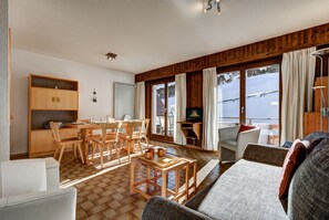 Uma sala ampla com uma mesa de jantar de madeira, cadeiras, um sofá e uma televisão.