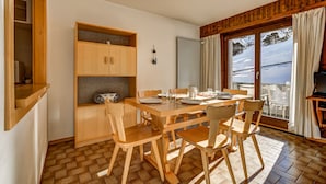 Un comedor con mesa y sillas de madera, un mueble de madera, y vista a un paisaje nevado a través de grandes ventanales.