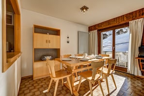 Uma sala de jantar com mesa e cadeiras de madeira, um armário de madeira e vista para uma paisagem nevada através de grandes janelas.