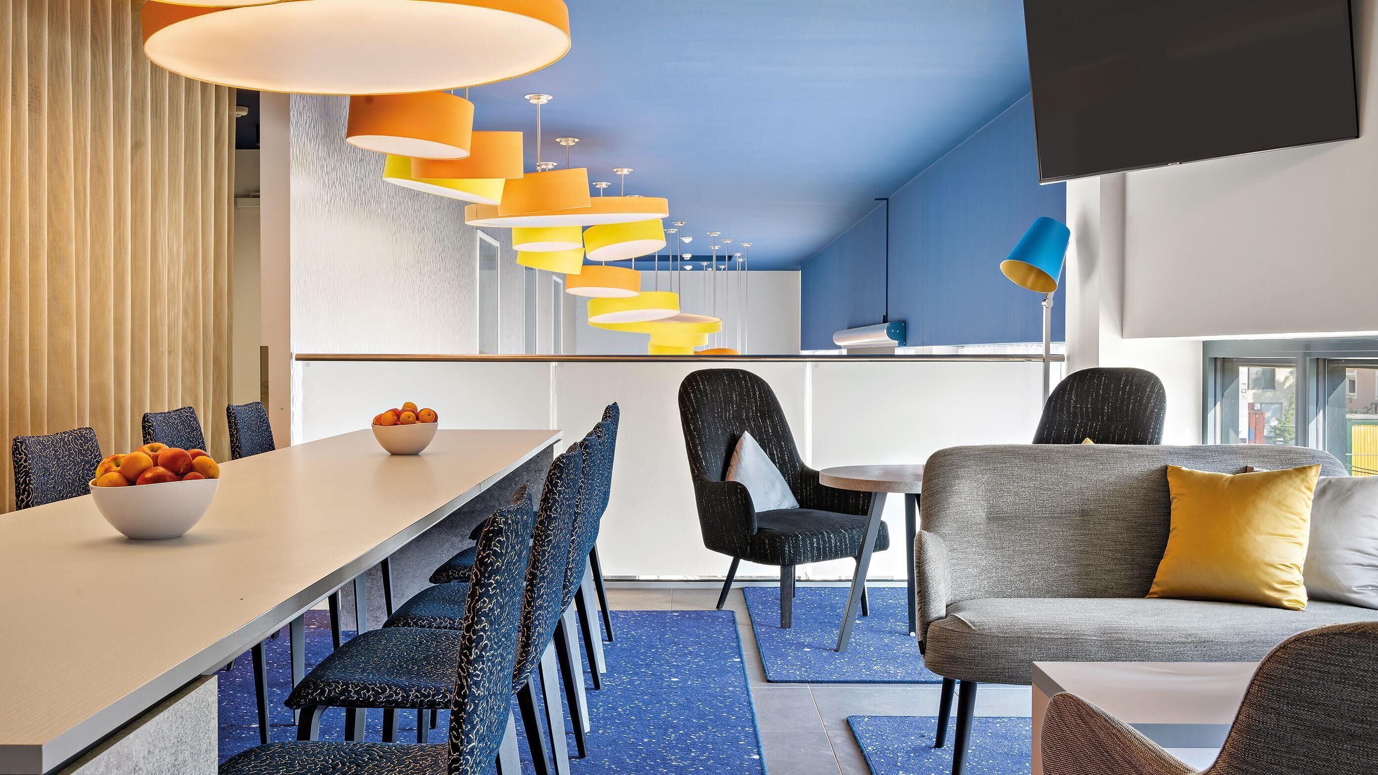 A modern kitchen with a dining area, featuring a long table, chairs, and a sofa.