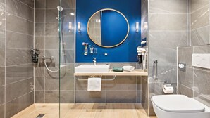 Un baño moderno con un espejo grande, un lavamanos, un inodoro y una zona de ducha.
