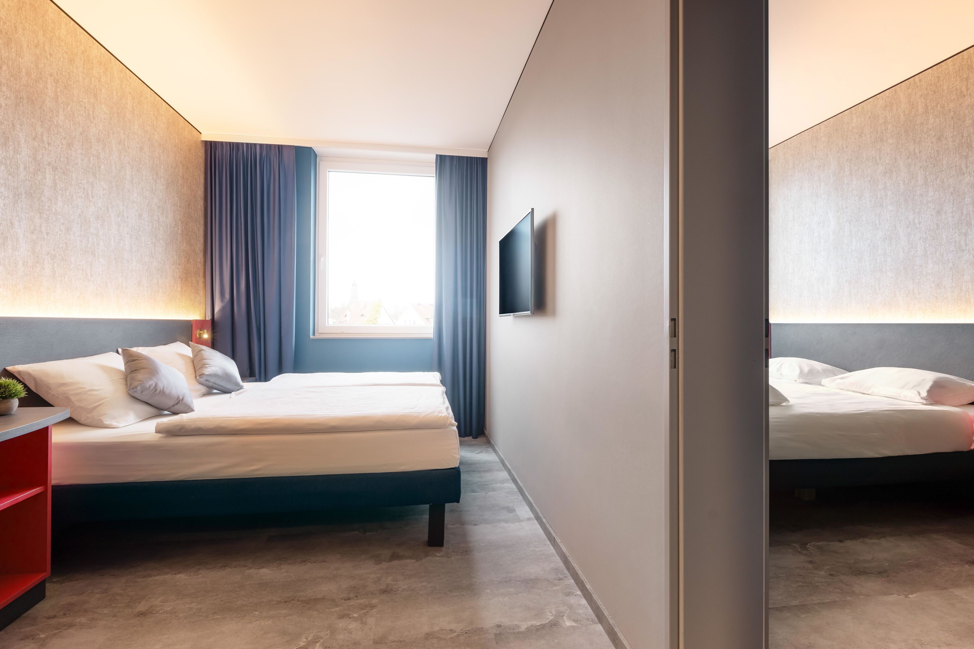A modern hotel room with a large bed, a flat-screen TV, and a window with curtains.