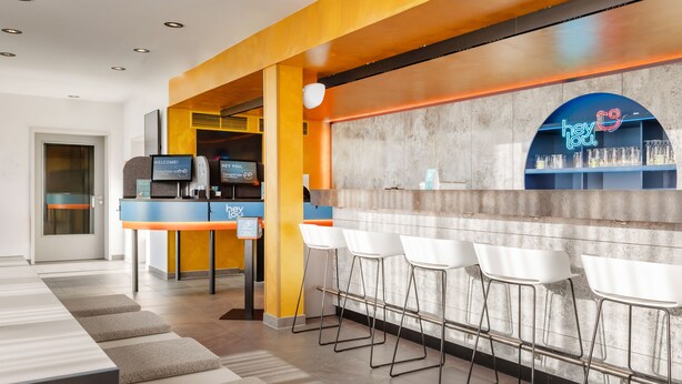 Un área de bar moderna con un letrero de neón, taburetes y una mesa de recepción.