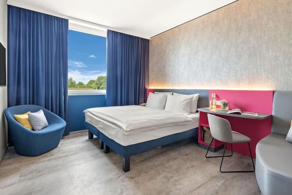 Habitación de hotel con cama, escritorio, silla y vistas al exterior.