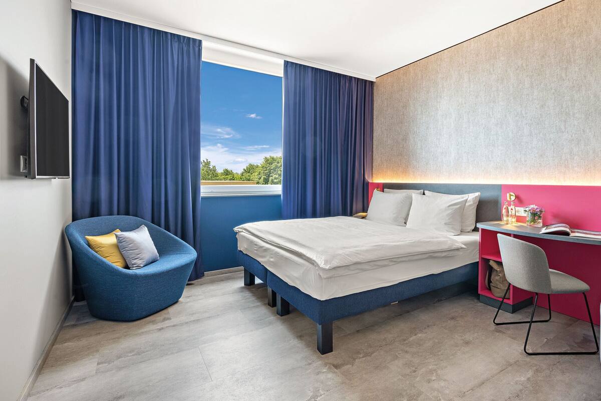 Een moderne hotelkamer met een bed, een bureau, een stoel en een televisie.