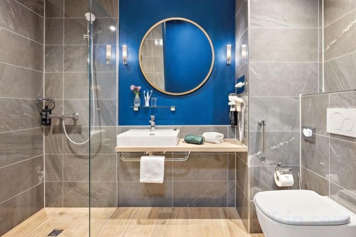 Un baño moderno con cabina de ducha de vidrio, un espejo redondo, un lavabo e inodoro.