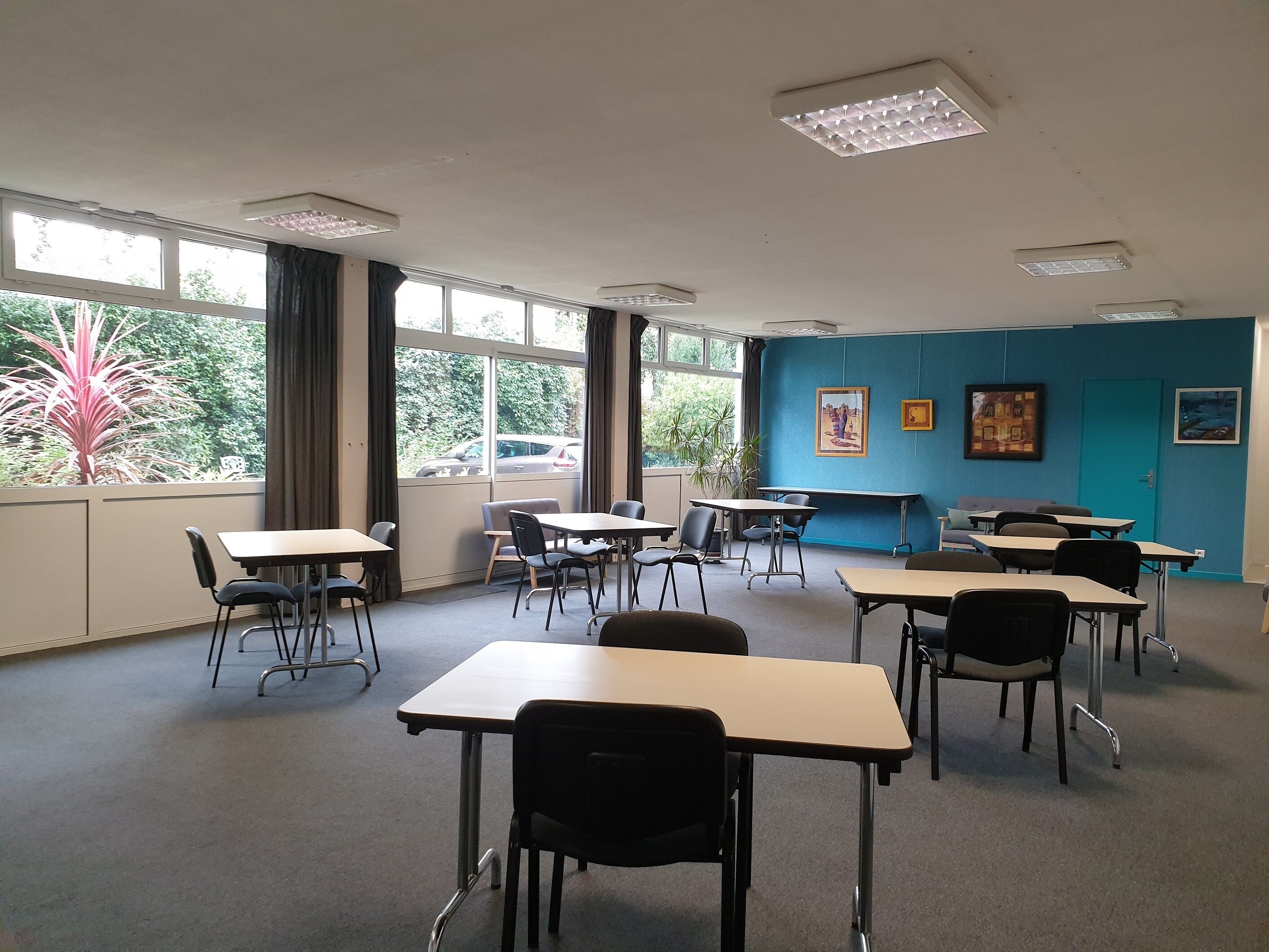 Un aula con escritorios y sillas dispuestos en filas, ventanas amplias con cortinas e iluminación en el techo.